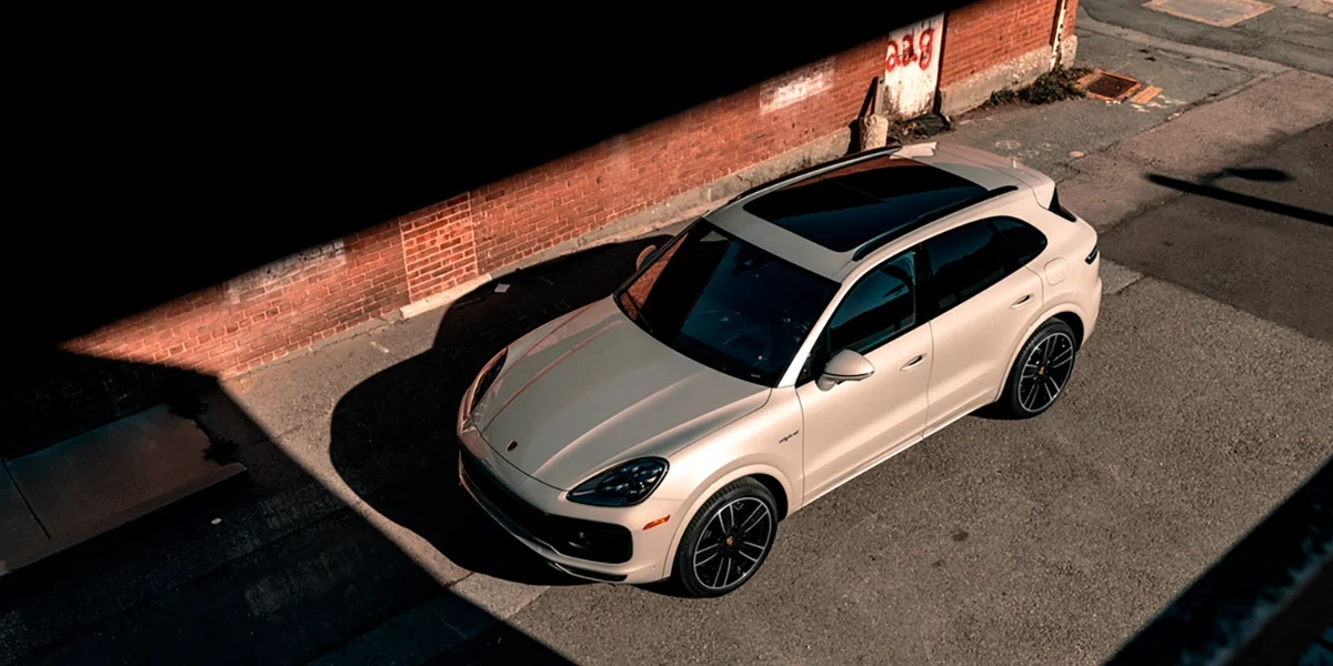 Beige Porsche Cayenne E-Hybrid parked beside a red brick wall in urban daylight – Porsche Marin dealership photography.
