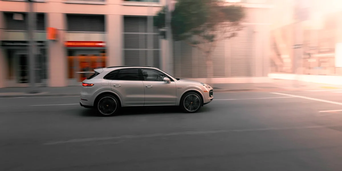 Silver Porsche Cayenne Turbo S driving through city streets at dusk – Porsche Marin high-performance SUV in motion.