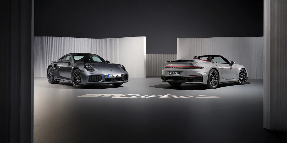 2026 Porsche 911 Turbo S lineup — grey coupe and white cabriolet convertible — luxury high-performance sports cars in studio setting.